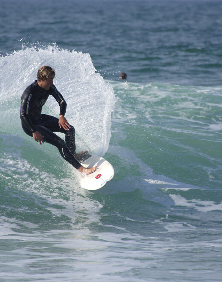 A person surfing. They are wearing a wet suit. They are on the face of the wave. Water is spraying up from under their board. They appear to be moving quickly.