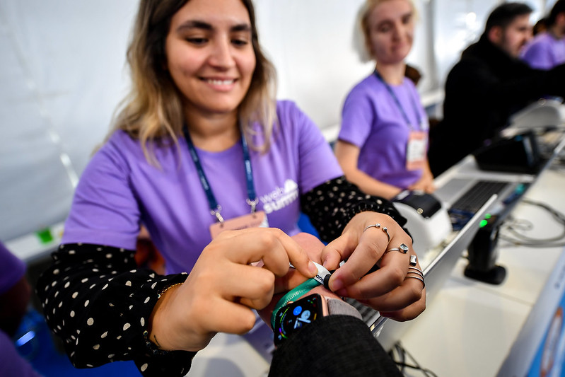 A smiling person attaches a wristband to the wrist of a person wearing an Apple watch. They are pictured from the point of view of the person whose wristband is being attached.