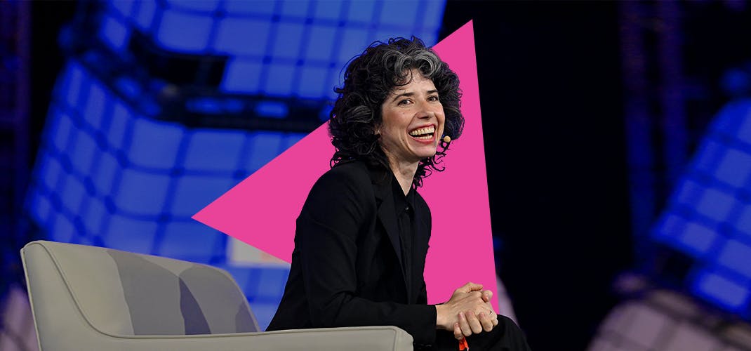 Meredith Whittaker, president of Signal, is sitting on stage with her hands clasped. Meredith's head is turned toward the audience and the CEO is smiling.