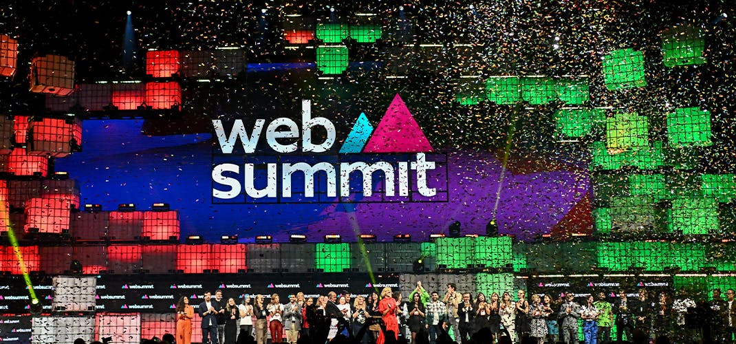 A crowd of people stand on a large stage, applauding. Above their heads, the Web Summit logo is clearly visible. Confetti falls from the ceiling. This is Web Summit 2023's closing ceremony