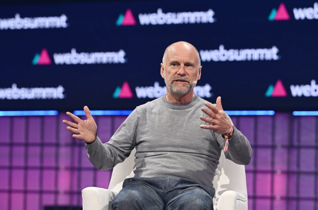 A person (Union Square Ventures managing partner Albert Wenger) sits in an armchair. The person is wearing a headset mic and is gesturing with both hands. They appear to be speaking. Behind them, the Web Summit logo is visible in several places. This is Centre Stage during Day 1 of Web Summit 2023 at the Altice Arena in Lisbon, Portugal.