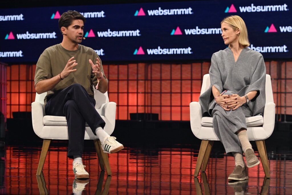 A person speaking and gesturing with their hands sits on the left, with another person sitting to the right. The Web Summit logo is visible in several places behind them. 