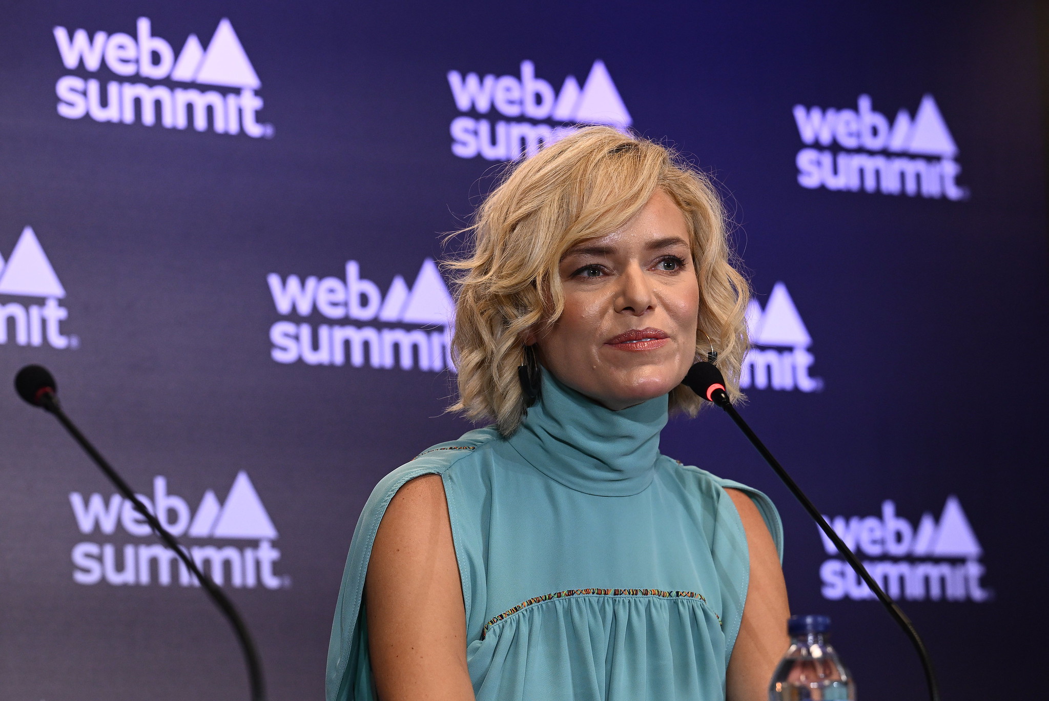 A person (Web Summit CEO Katherine Maher) pictured in front of a wall that features the Web Summit logo prominently in several places. Katherine is seated behind a small microphone. This is a press conference at Web Summit 2023 in Lisbon.
