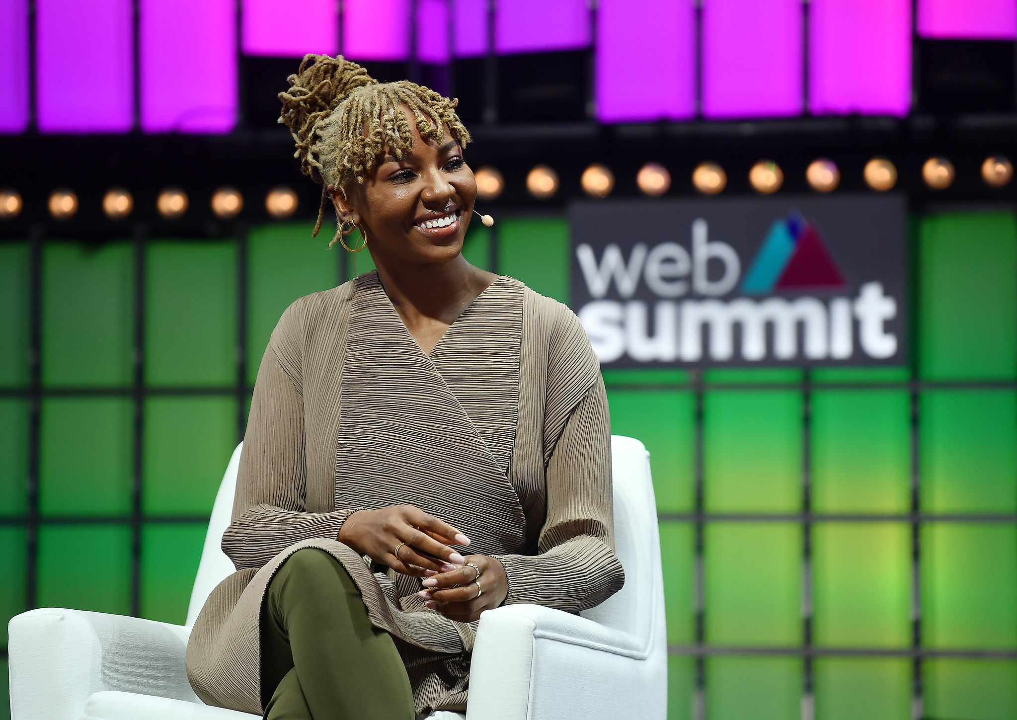 Photograph of a person (Ayọ Tometi, co-founder of Black Lives Matter) speaking on Centre Stage at Web Summit. The person is sitting on a chair and smiling. The Web Summit logo appears in the background.
