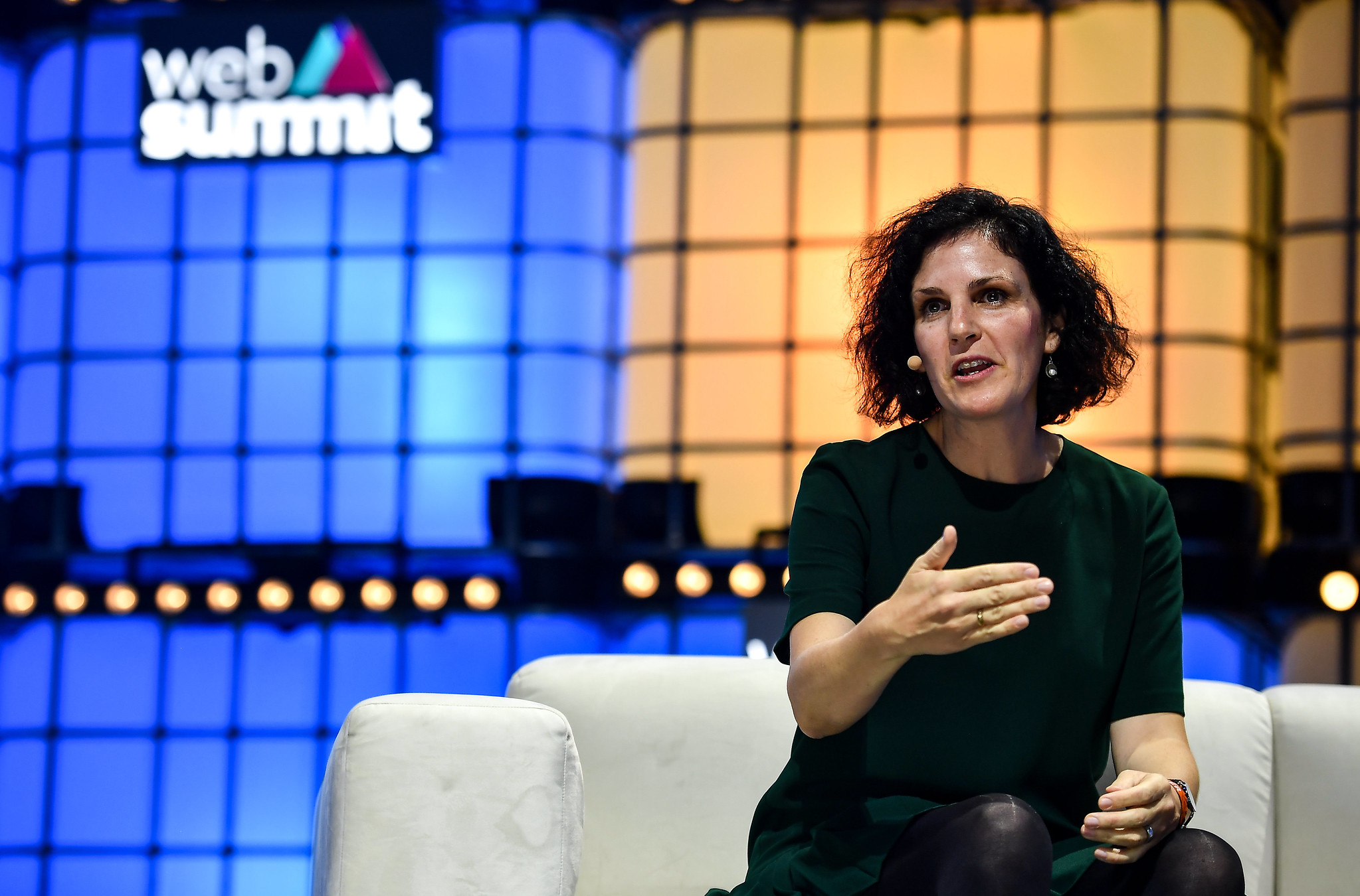 A photograph of Barbara Martin Coppola, former chief digital officer of IKEA, speaking on Centre Stage at Web Summit. Barbara is sitting on a chair and appears to be speaking. Barbara is gesturing with hands to speak and appears to be wearing an on-ear microphone. The Web Summit logo is visible in the background.