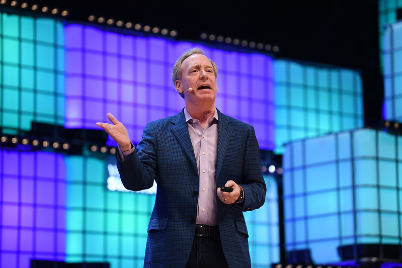 A photograph of Brad Smith speaking on Centre Stage at Web Summit. Brad is gesturing to the audience and wearing an on-ear microphone.