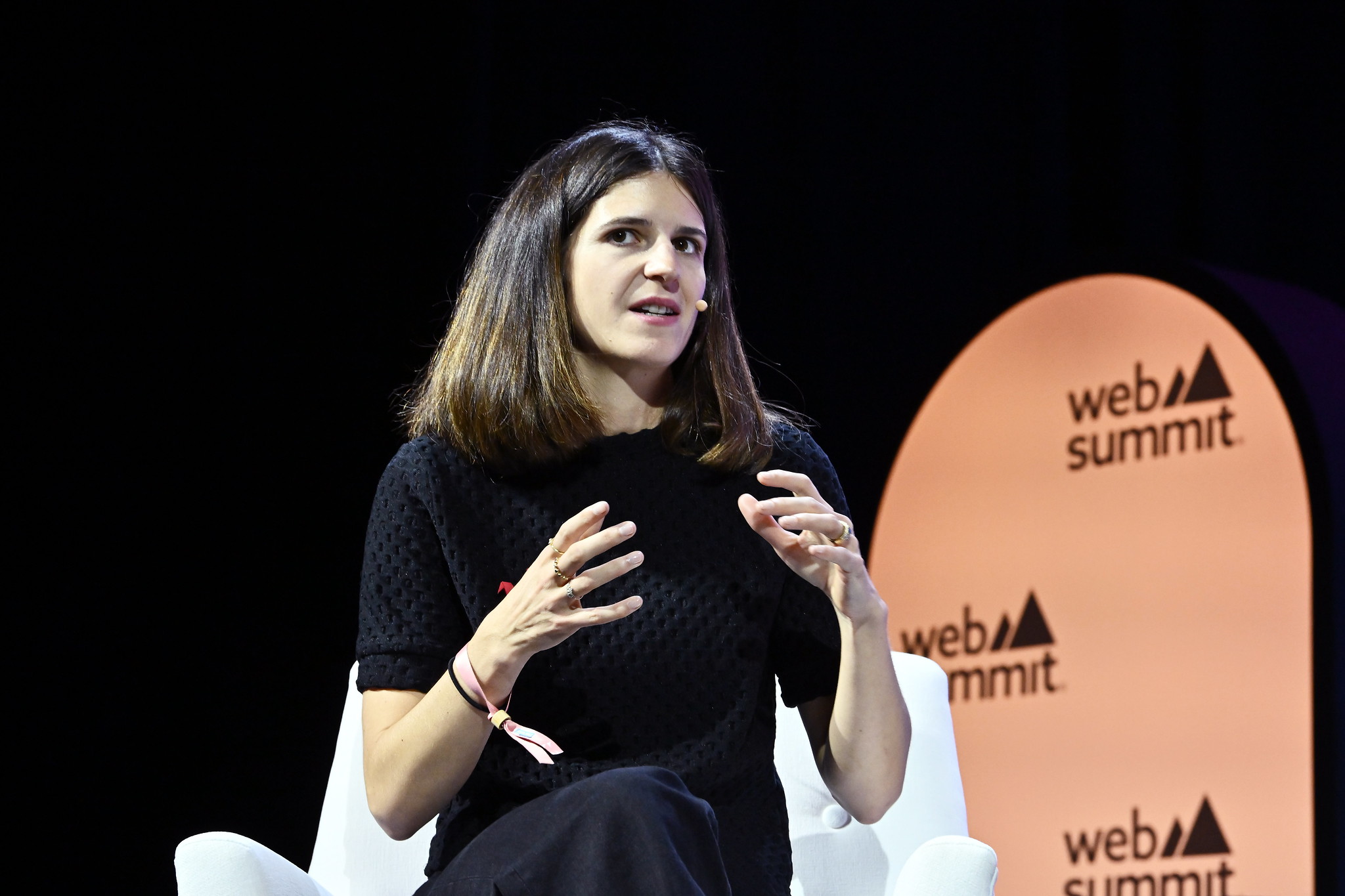 A photograph of Clara Chappaz, director of La French Tech, speaking on the Startup University stage at Web Summit. Clara is sitting on a chair and appears to be speaking, looking away from the camera and towards the crowd. The background is dark and features the Web Summit logo.