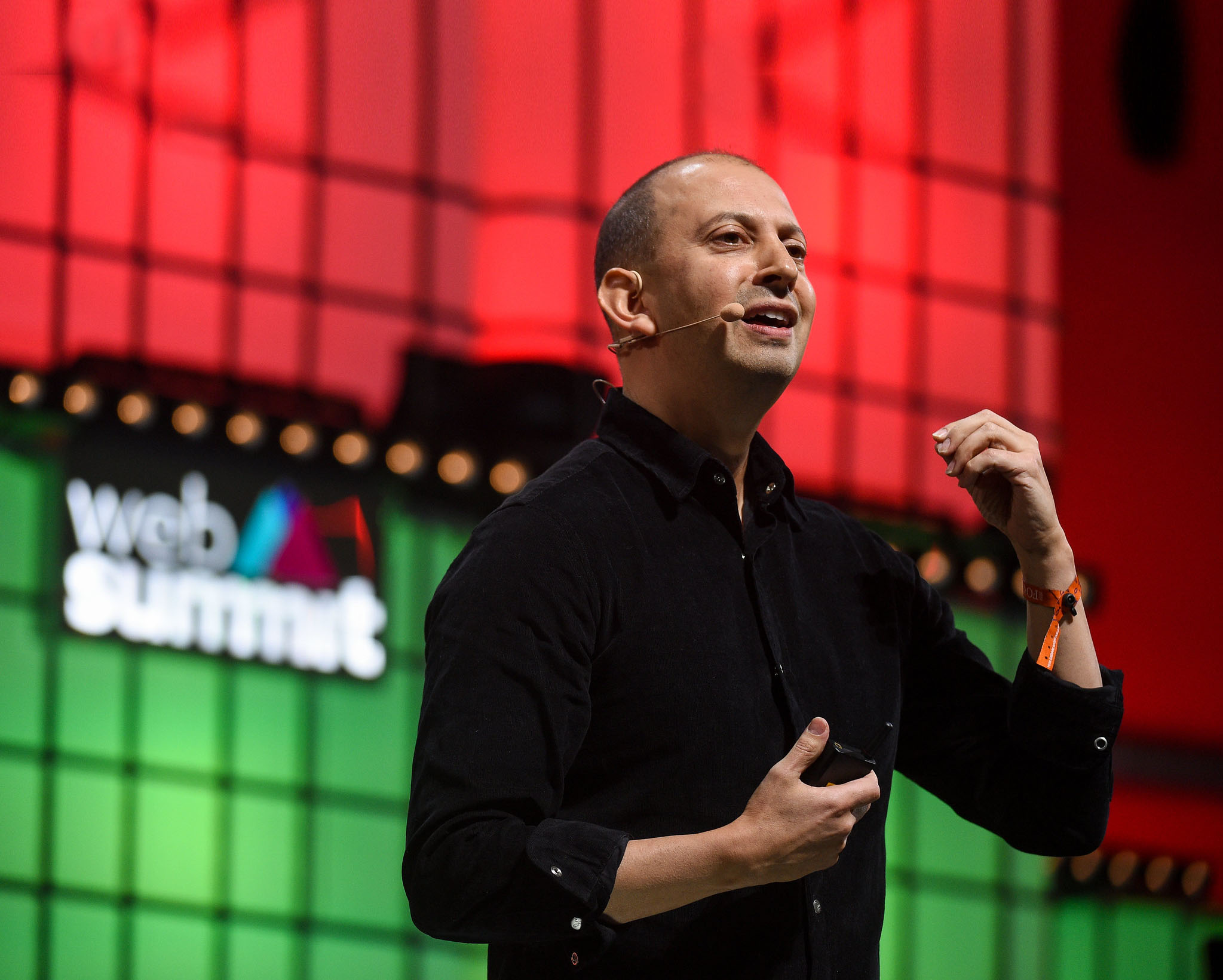 A photograph of David Wallerstein, chief exploration officer at Tencent Holdings, speaking on Centre Stage at Web Summit. David is gesturing using hands, and appears to be speaking to a crowd. David is wearing an on-ear microphone. The photograph is zoomed-in, and only the upper section of David's body is visible.