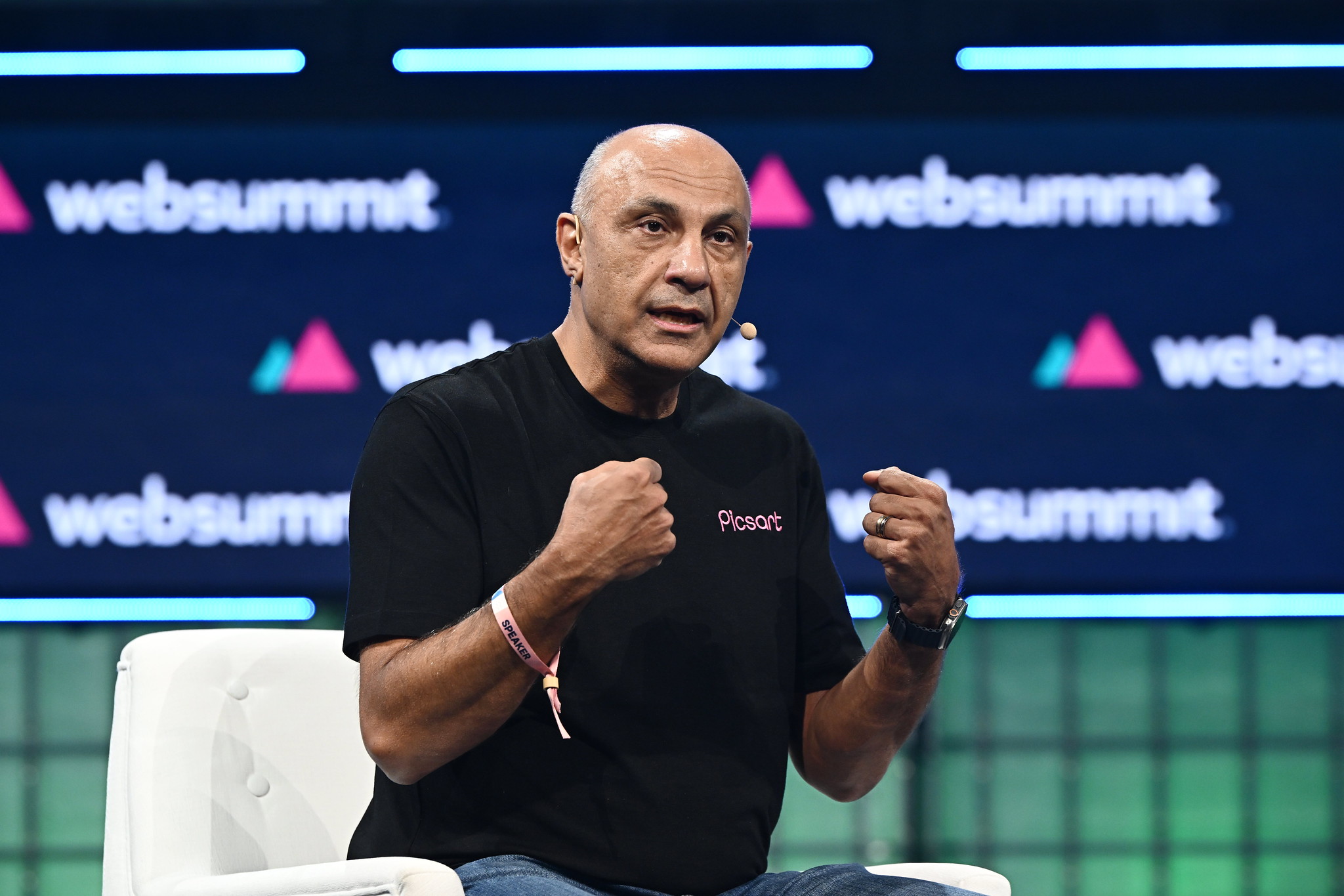 Photograph of a person (Hovhannes Avoyan, Founder and CEO of Picsart) speaking on stage at Web Summit. The person is sitting on a chair and gesturing with their hands.