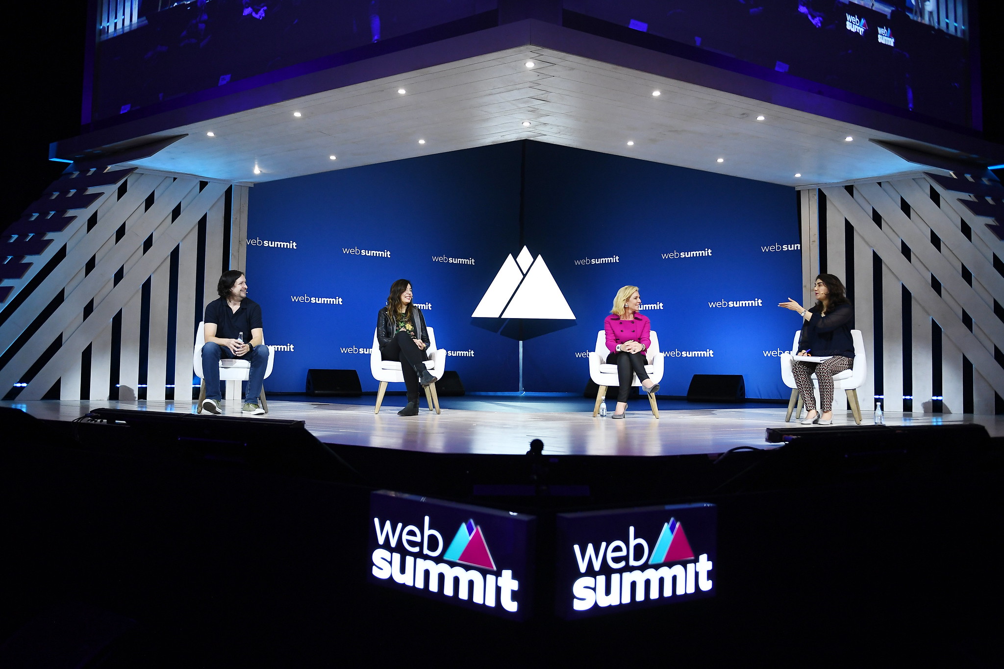 A photograph of four speakers (Jager McConnell, Mada Seghete, Christal Bemont, and Alisa Cohn) sitting on stage at Web Summit. They appear to be having a panel discussion. The photograph is zoomed out, and the entire stage is visible. There are two Web Summit logos beneath the stage.