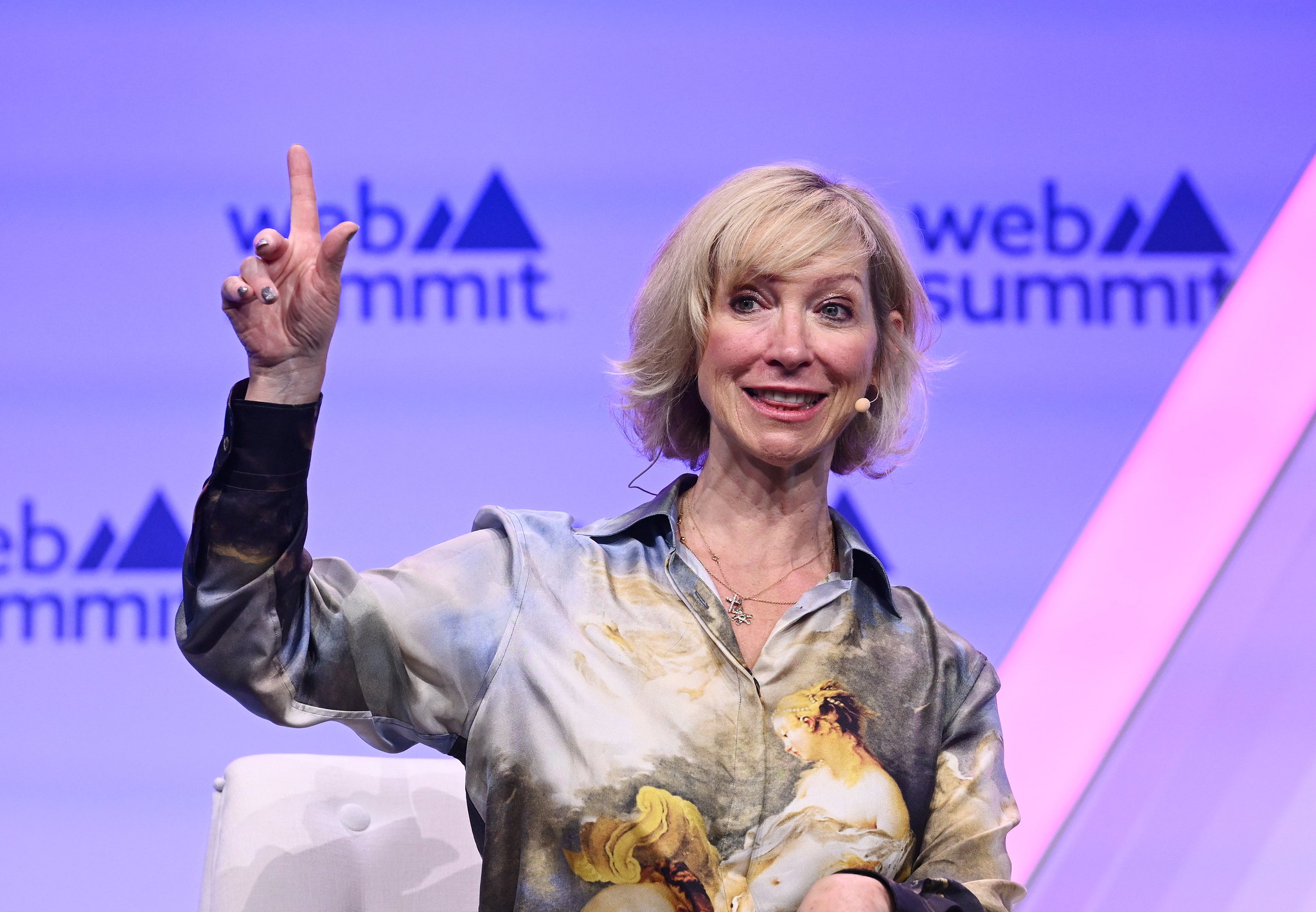 A photograph of a person (Janet Adams, COO of SingularityNET) on stage at Web Summit. The person has one finger pointed in the air. They appear to be speaking.