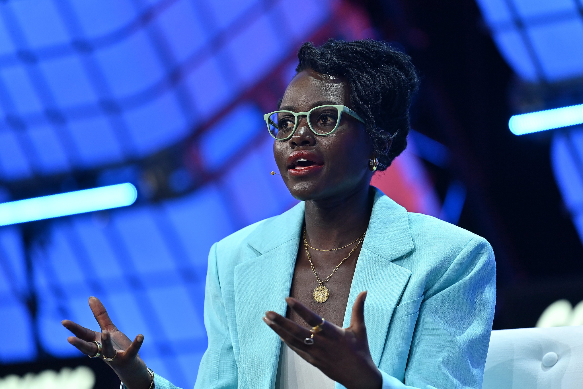 Photograph of a person (Actor Lupita Nyong‘o) speaking on stage at Web Summit. The person is gesturing with their hands.