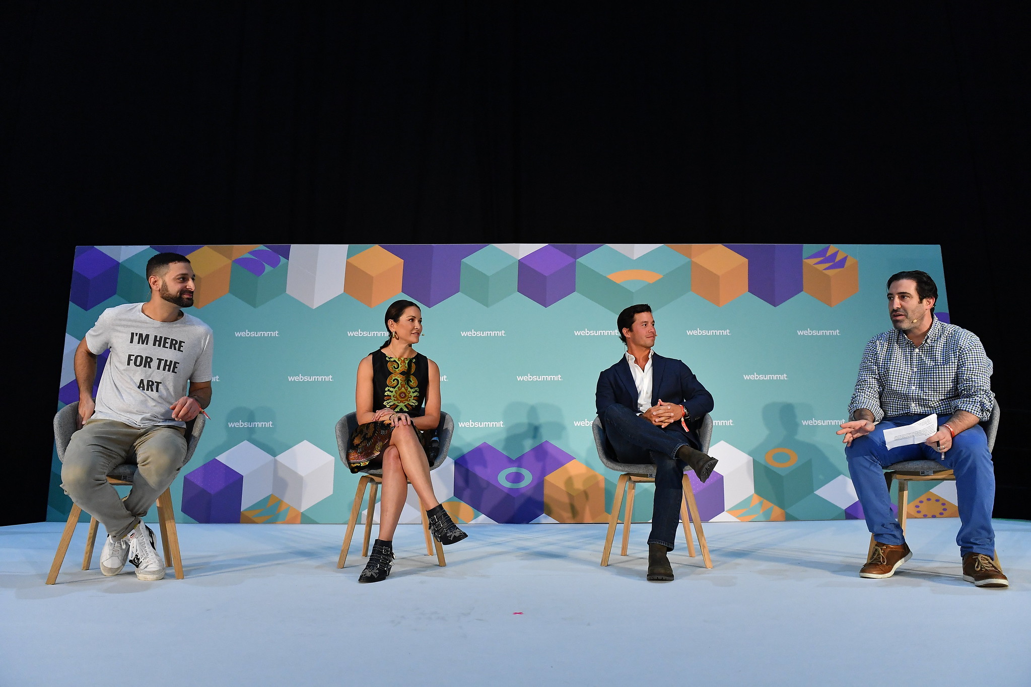 A photograph of four people speaking on stage at Web Summit. They are seated and appear to be having a discussion.