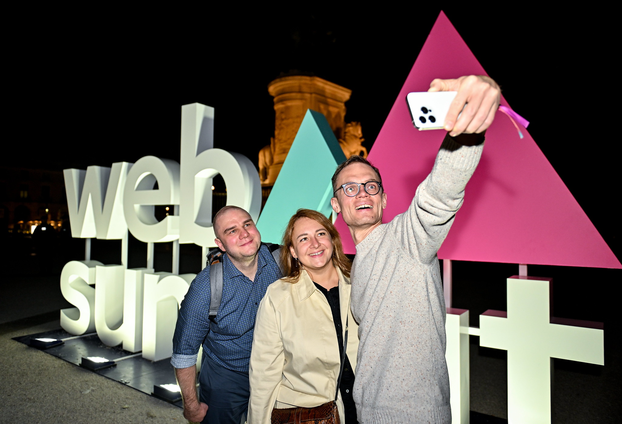 Smiling night summit attendees take a selfie in front of a large Web Summit sign