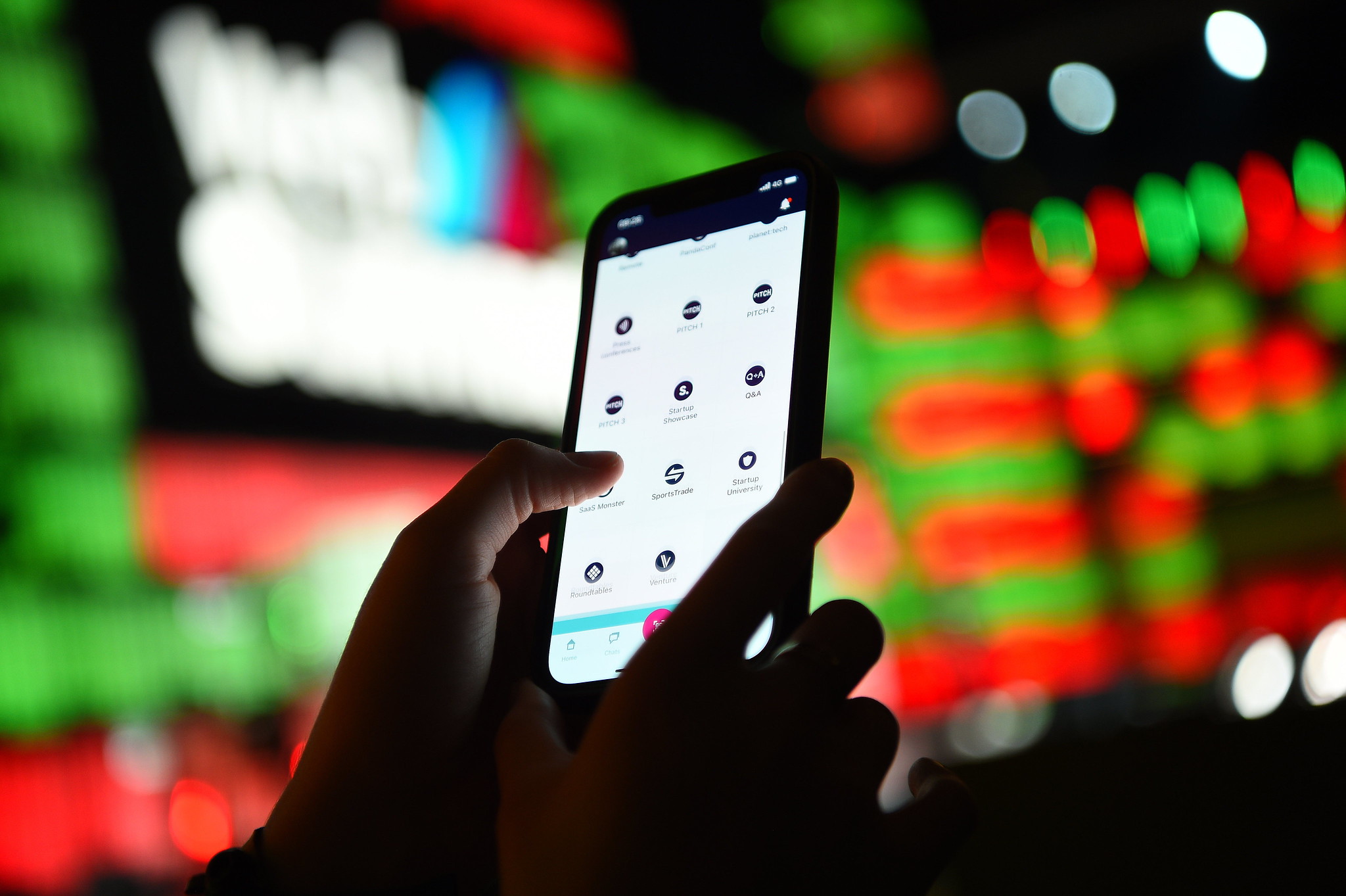 A zoomed-up photograph of hands holding and using a smartphone. Web Summit’s Centre Stage is visible in the background.